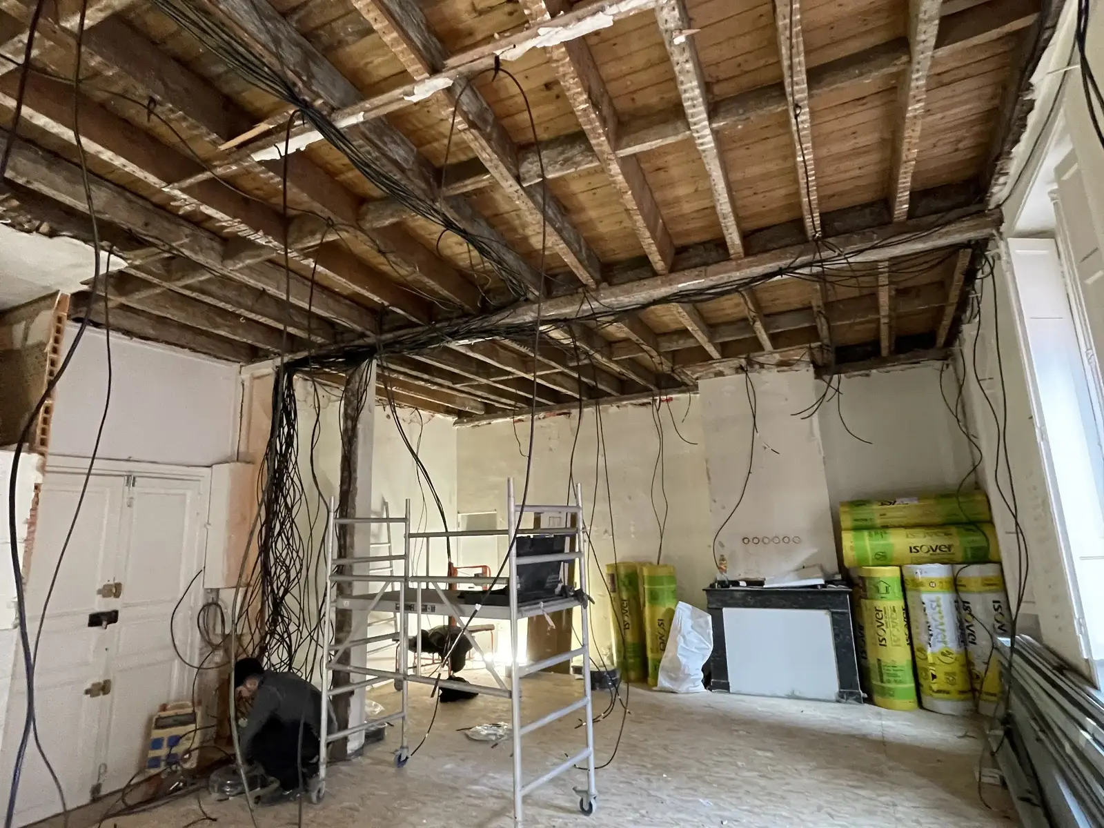 Pièce en chantier aux solives apparentes, câbles pendants, rouleaux d’isolant et échafaudage sur un sol brut