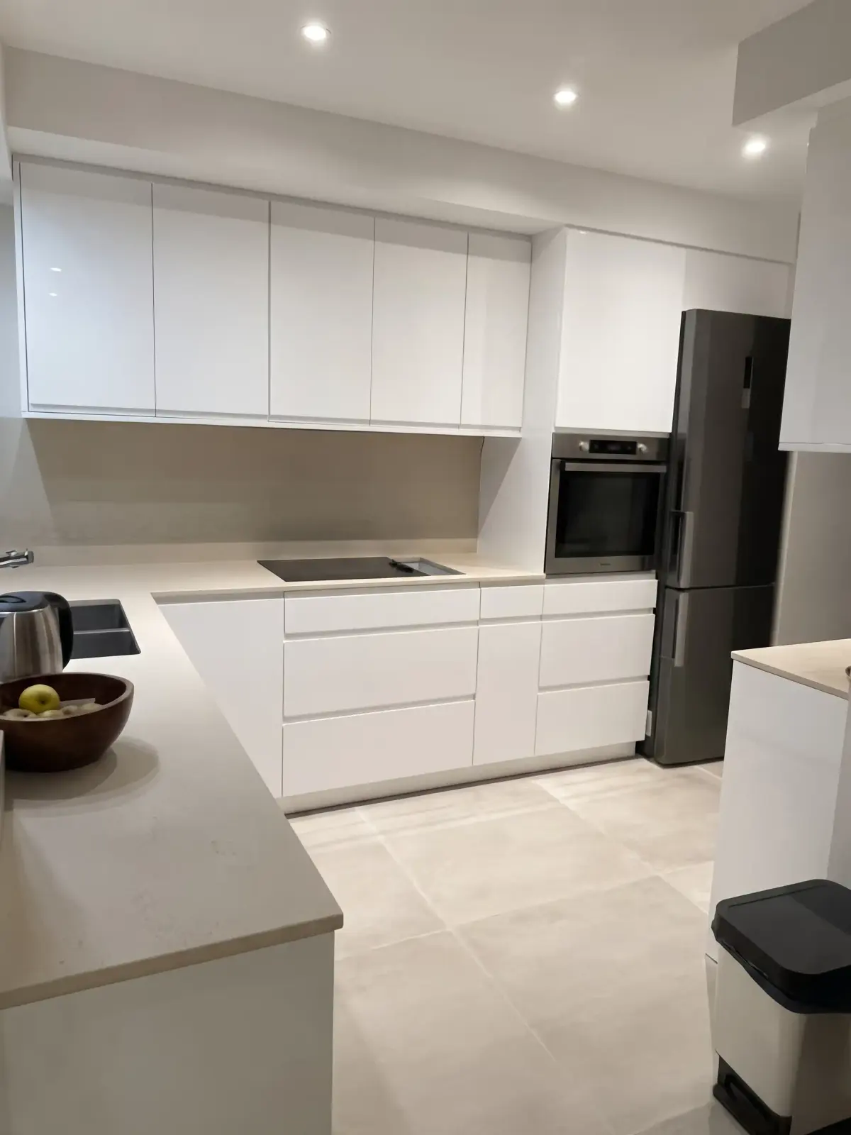 Cuisine aux façades blanches laquées, plan de travail gris, four encastré et spots au plafond