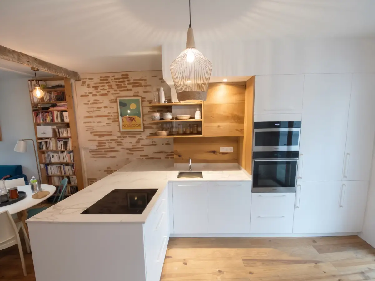Cuisine ouverte en U aux façades blanches, niche en bois et mur de briques, sur parquet clair