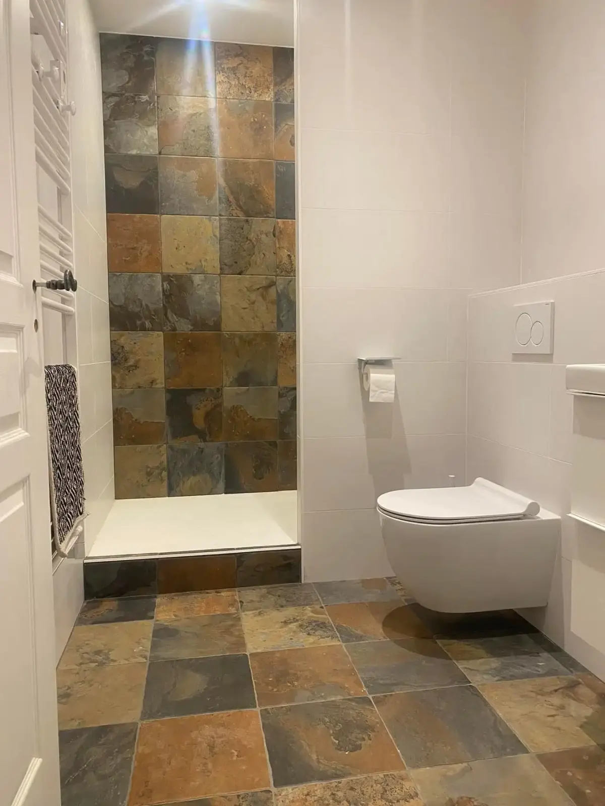 Douche à l’italienne avec paroi en ardoise multicolore, WC suspendu et sol en ardoise