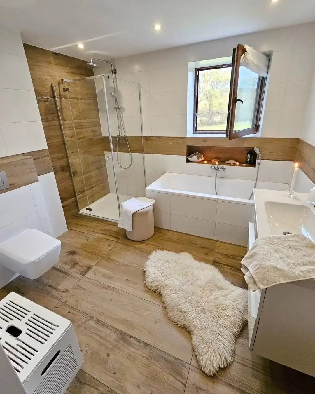 Salle de bain habillée de panneaux bois et de carreaux gris, miroir rond et meuble vasque blanc suspendu