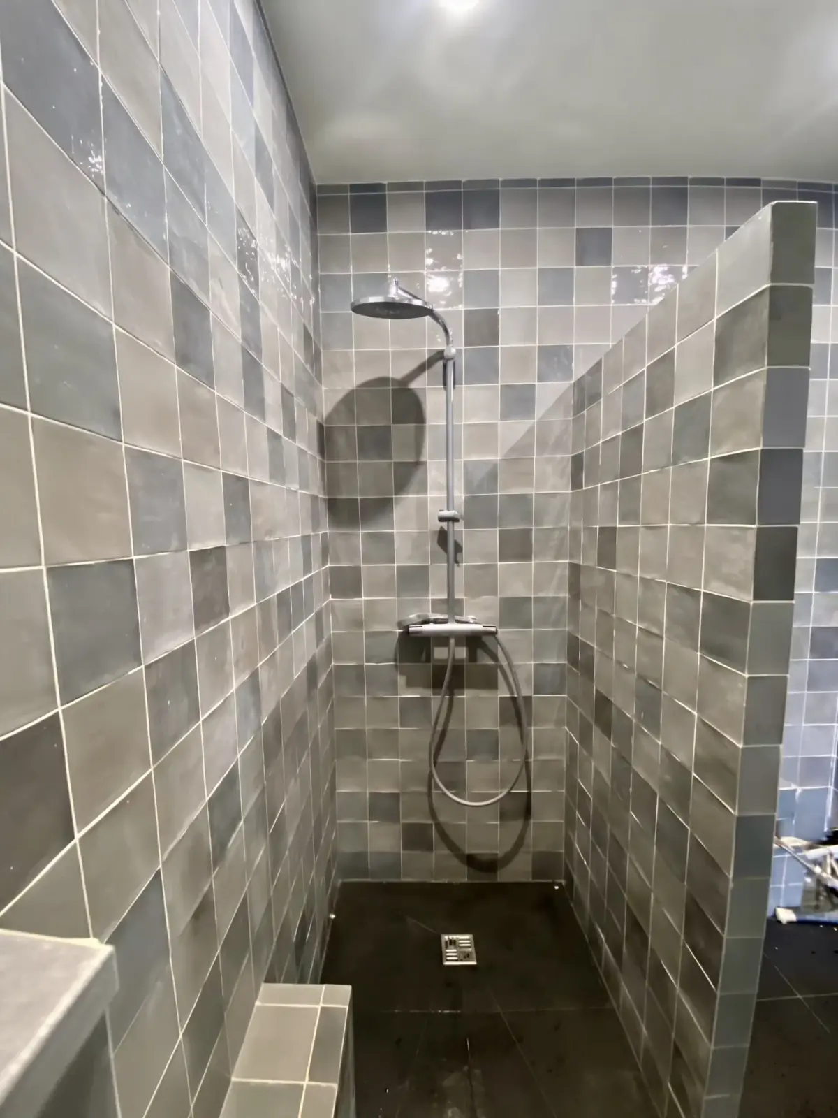 Douche à l’italienne habillée de carreaux irréguliers gris-bleu, avec douchette murale
