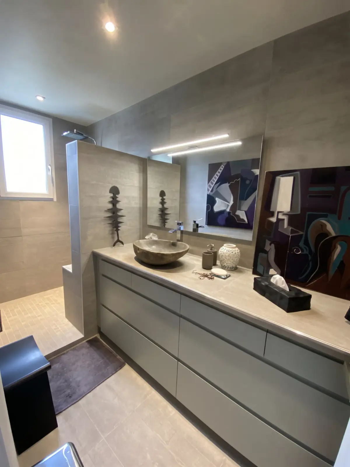 Salle de bain aux murs gris, meuble gris à tiroirs avec vasque en pierre et douche à l’italienne